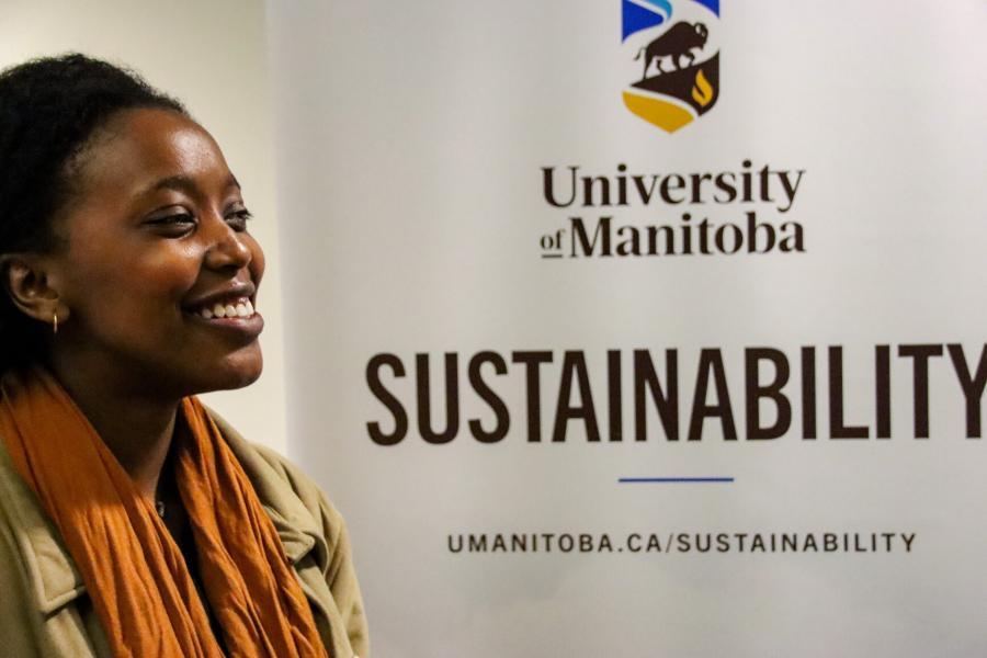 A student standing in front of a University of Manitoba Sustainability banner display.
