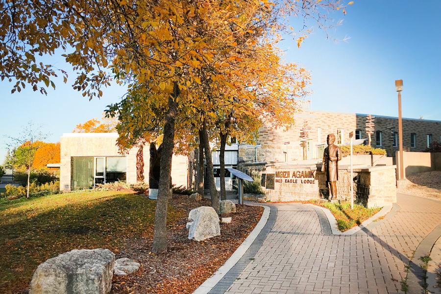 Exterior view of the Migizii Agamik - Bald Eagle Lodge up a pathway lined with trees to the front entrance.