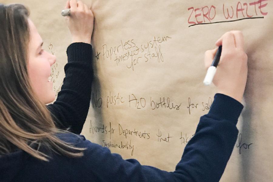 UM student writing a sustainability suggestion on a brown paper board display