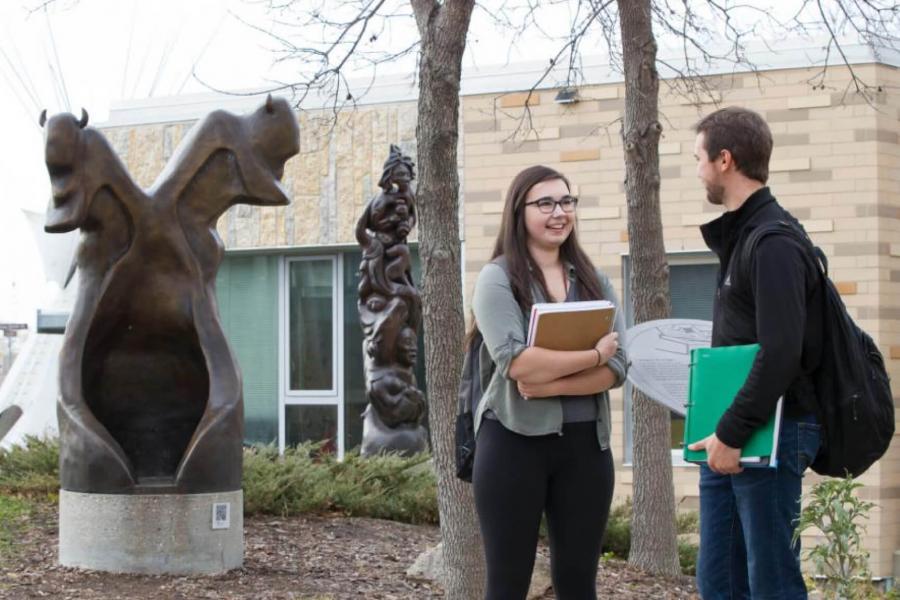 Two indigenous students stand together talking outside of the Migizii Agamik Bald Eagle Lodge.