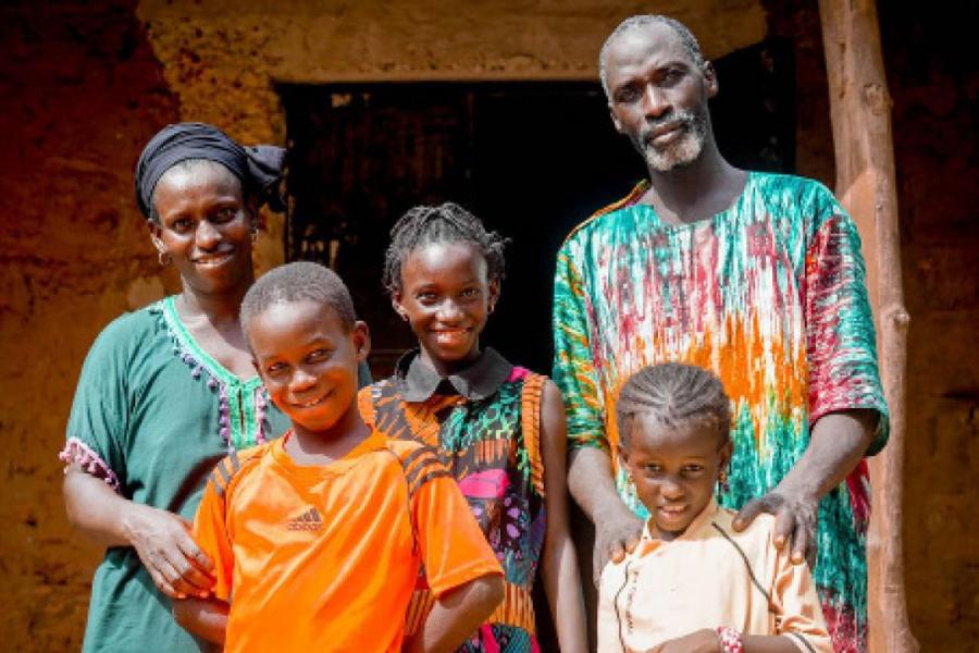 A Senegalese couple stands with their three children. They are wearing colourful outfits and smiling.
