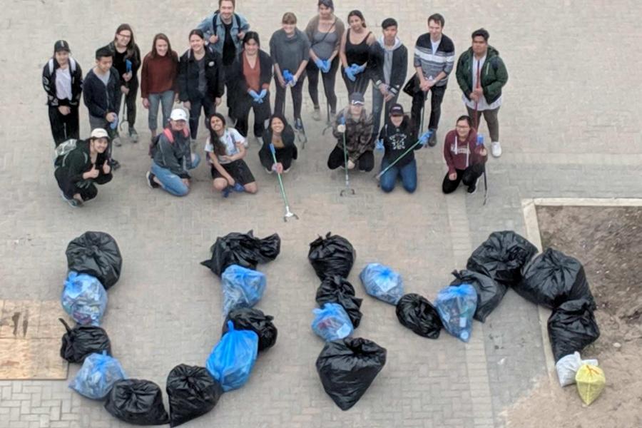 A group of students stand with trash bags and recycling bags that are positioned to spell out the letters U and M.