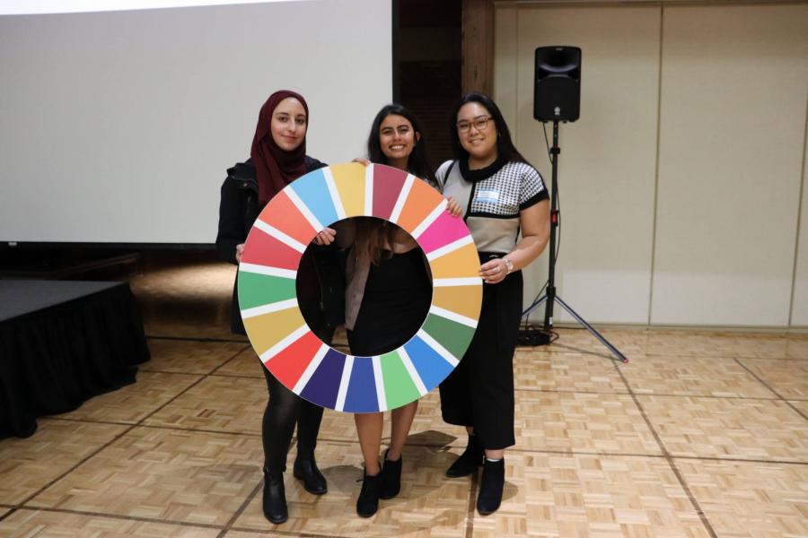 A group of three students stand with a large colourful circle cut-out.