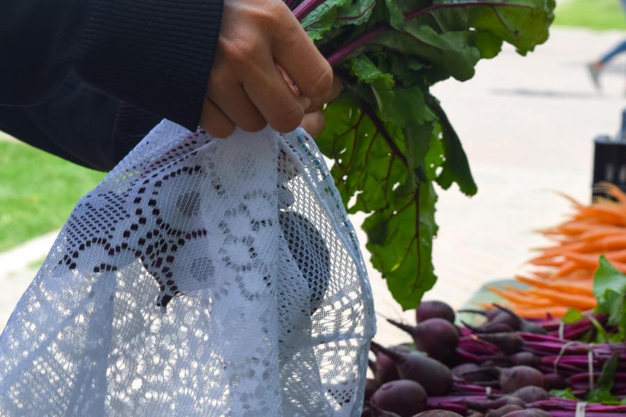A closeup of a persons hands putting vegetables into a reusable bag. 