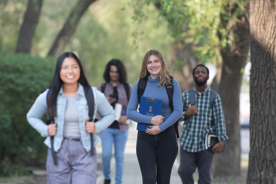 Four university of Manitoba students walking while carrying school books and supplies.